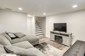 A living room with a grey sofa, a television on a wooden cabinet, and a staircase in the background. - Walk to Fairmount Park: Modern Philly Townhome! (Philadelphia)