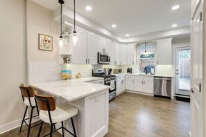 A modern kitchen with white cabinetry, a large island with bar stools, stainless steel appliances, and pendant lighting. - Walk to Fairmount Park: Modern Philly Townhome! (Philadelphia)