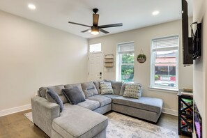 A living room with a sectional sofa, ceiling fan, windows, and a mounted TV. - Walk to Fairmount Park: Modern Philly Townhome! (Philadelphia)