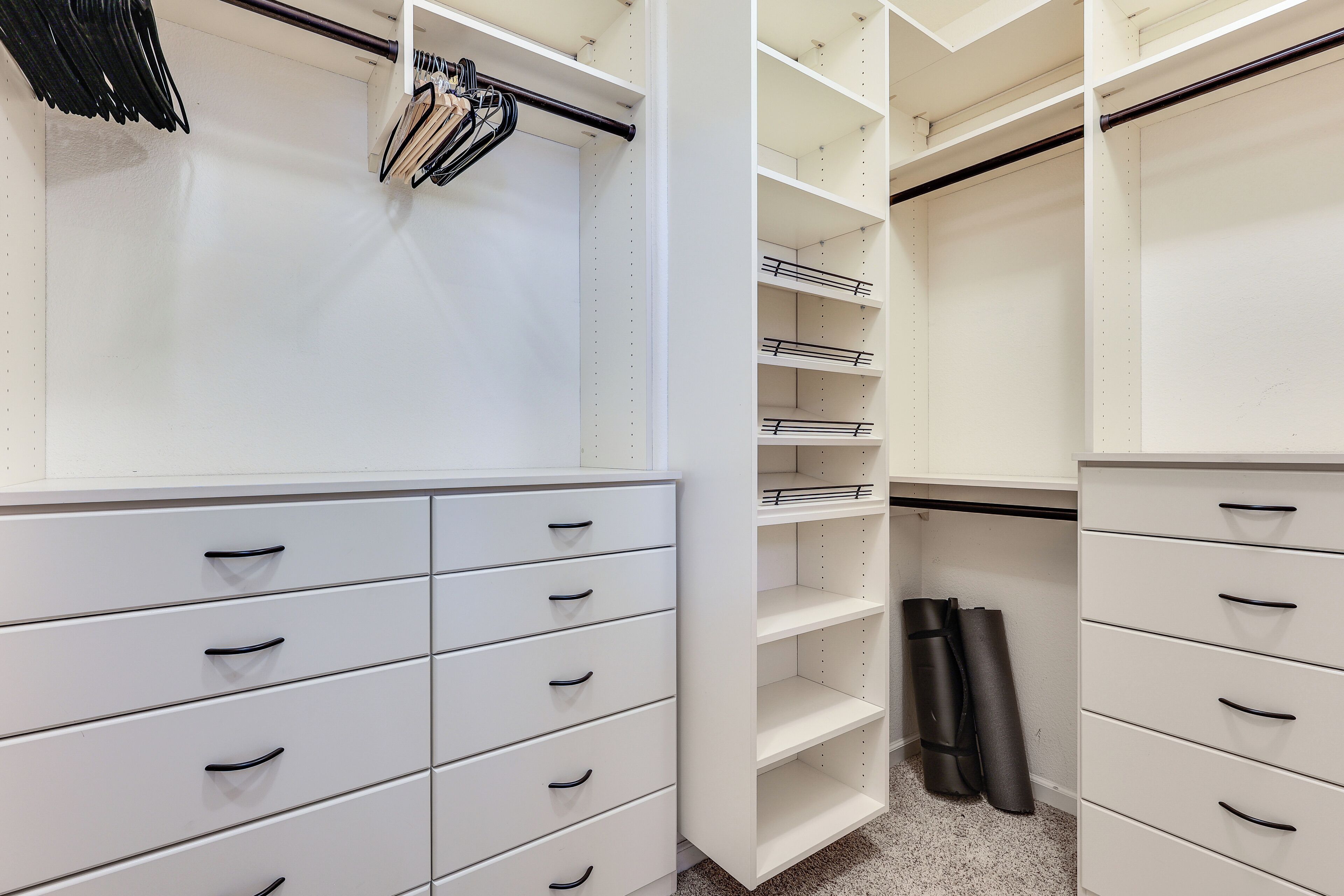 A white closet with multiple drawers and shelves, a hanging rod, and a pair of black shoes on the floor.