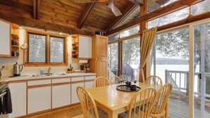 Un interior de madera con una mesa de comedor, sillas, una zona de cocina y ventanas amplias.