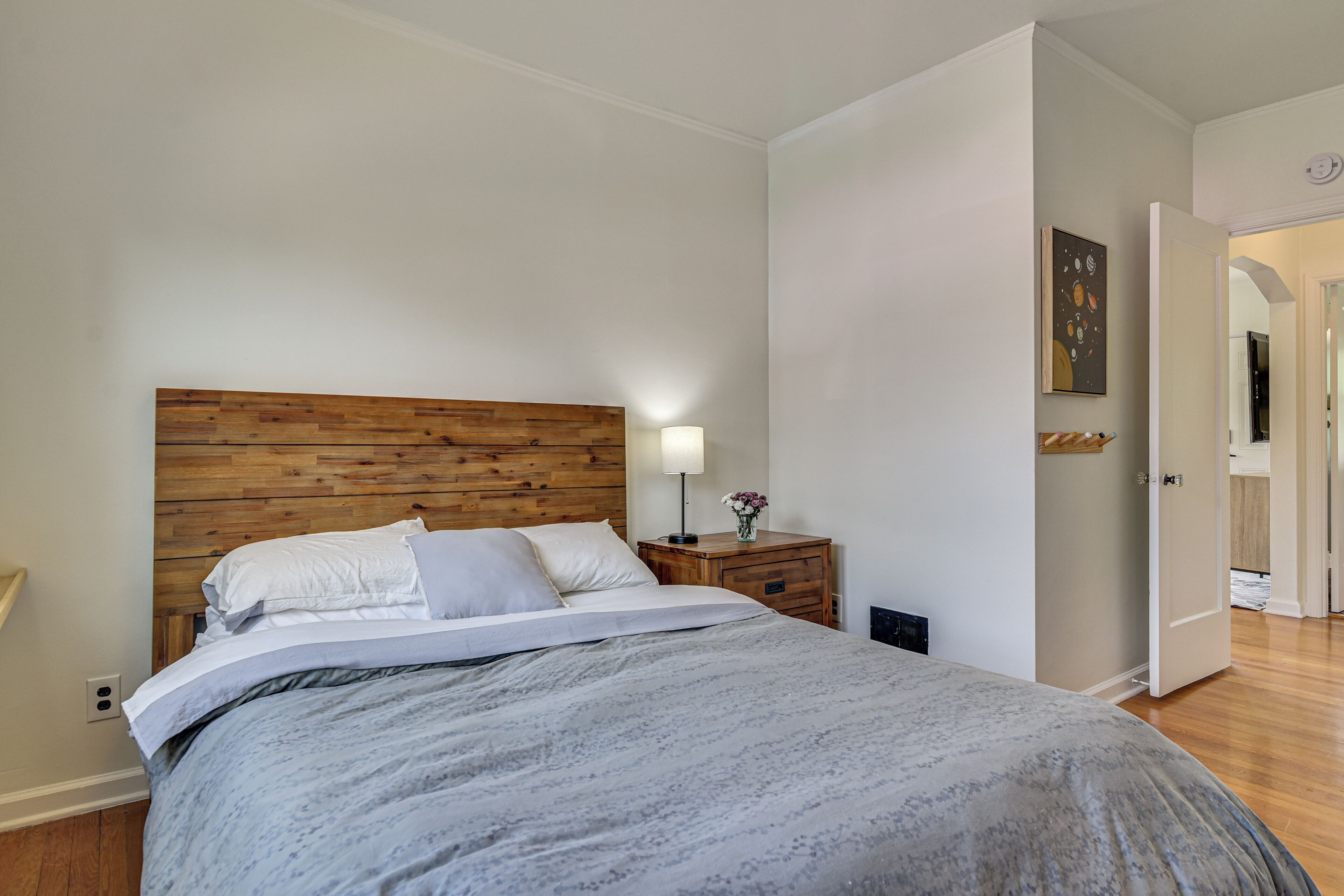 Ein Schlafzimmer mit Holzkopfstütze, einem Nachttisch mit Lampe und einer Tür zu einem anderen Raum.