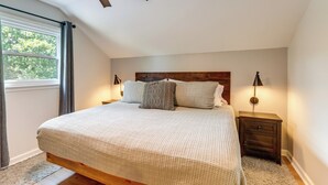 Ein Schlafzimmer mit Bett, Nachttischen, Deckenventilator, Fenster und Blick auf Bäume.