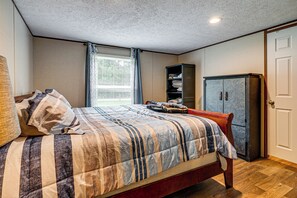 Un dormitorio con cama, armario, ventana con cortinas y lámpara en el techo.