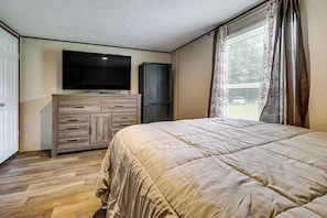Ein Schlafzimmer mit einem Bett, einem an der Wand befestigten Fernseher, einem Kleiderschrank und einem Fenster mit Vorhängen.