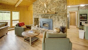 A cozy living room with a stone fireplace, wooden ceiling, and a view of the outdoors. - Mountain Views + BBQs: Updated Cody Cabin (Cody)
