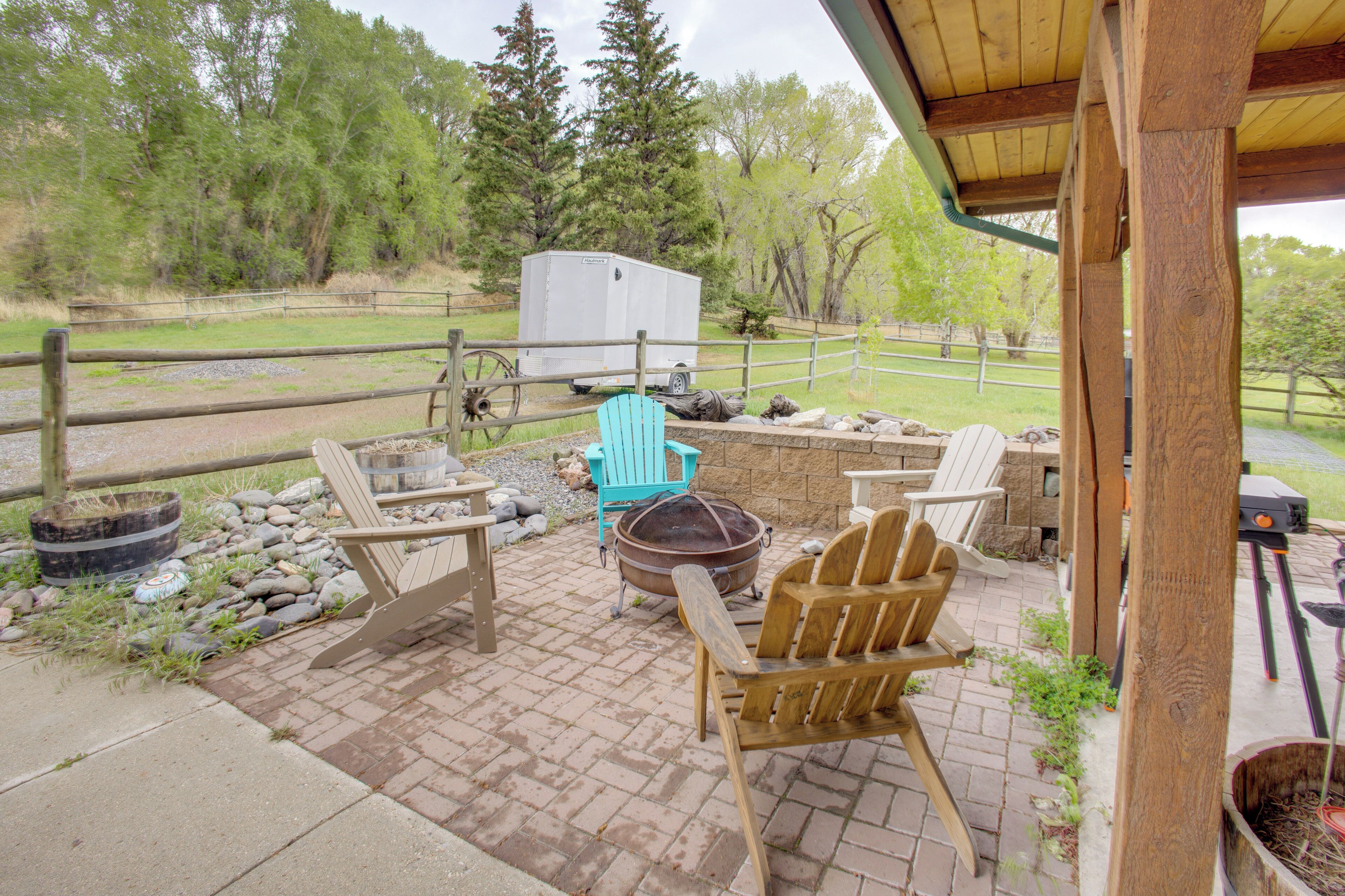Une terrasse extérieure avec des chaises en bois, un foyer et une remorque blanche.