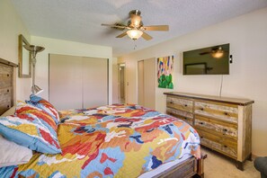 A bedroom with a bed, a ceiling fan, a dresser, a painting, and a television.