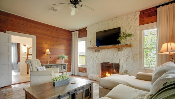 A living room with a stone fireplace, a television mounted on the wall, and a ceiling fan. - Pet-Friendly Historic Home: Downtown Breaux Bridge (Breaux Bridge)