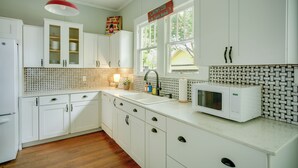 A kitchen with white cabinets, a microwave, a sink, and a window with a view of the outside. - Pet-Friendly Historic Home: Downtown Breaux Bridge (Breaux Bridge)