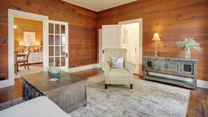 A room with wooden walls, a white door, a beige armchair, a wooden coffee table, and a cabinet with a lamp. - Pet-Friendly Historic Home: Downtown Breaux Bridge (Breaux Bridge)