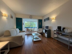 A modern living room with a sofa, coffee table, TV, and kitchenette. - La Brise Marine - Downtown - Port view (CAP BRETON)