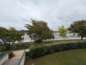 A waterfront park with trees, a pathway, and a view of boats on the water. - La Brise Marine - Downtown - Port view (CAP BRETON)