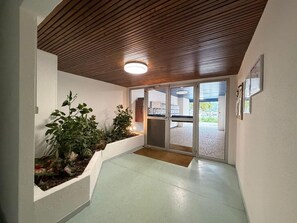 A hallway with a wooden ceiling, potted plants, and a glass door leading outside. - La Brise Marine - Downtown - Port view (CAP BRETON)
