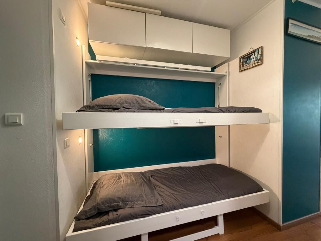 Una cama litera con una cama inferior, un armario blanco arriba y una pared de acento color aguamarina.