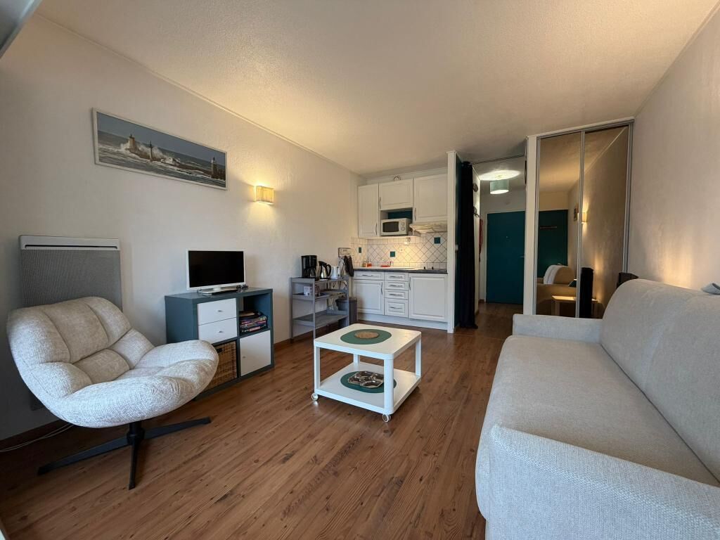 A compact living space with a sofa, a chair, a small table, a TV, and a kitchenette.