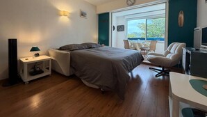 Een slaapkamer met een bed, nachtkastje, lamp, stoel, bureau en een raam met uitzicht.