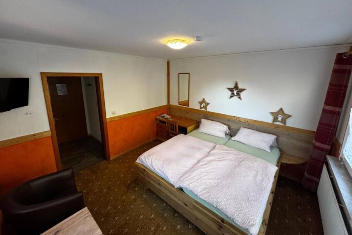 A single-bed room with a wooden headboard, a bedside table, a mirror, and a wall-mounted star decoration.