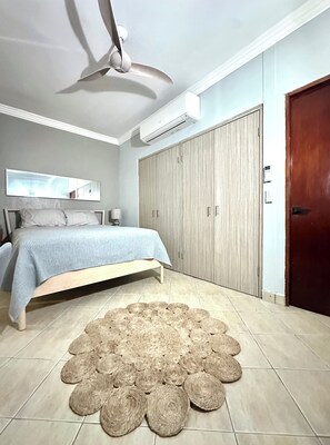 Ein Schlafzimmer mit Bett, Deckenventilator, Klimaanlage, Kleiderschrank und einem gewebten Teppich.