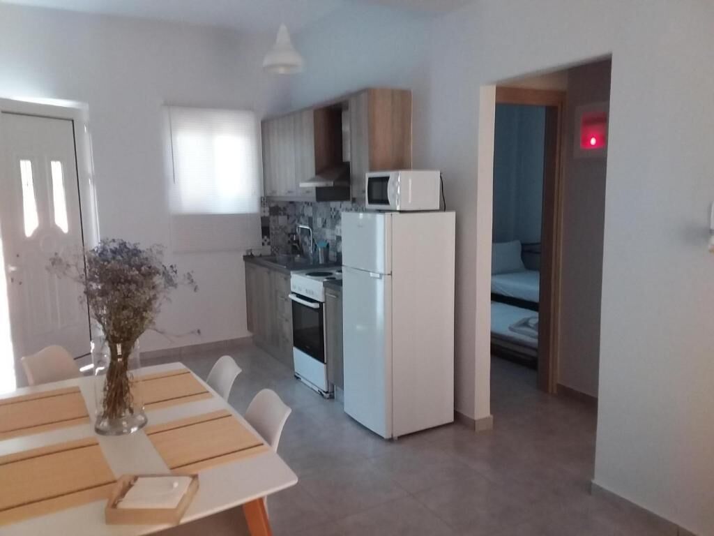 A modern kitchen with white appliances, a dining table with placemats, and a vase with flowers.