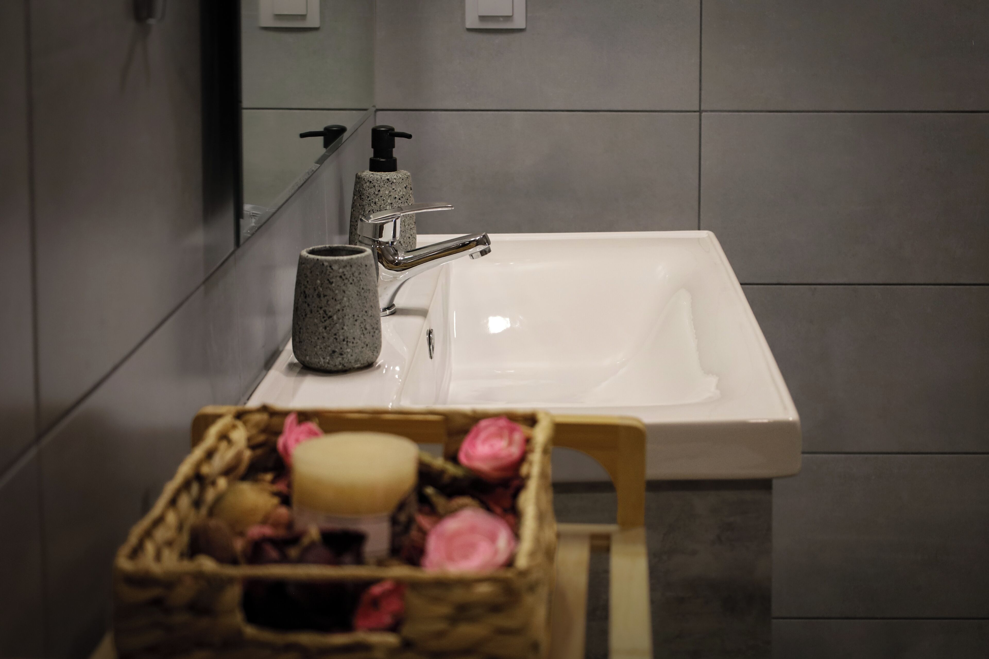 A bathroom with a white sink, a mirror, and a basket of toiletries.