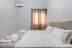 Habitación de hotel con cama, cabecera, ventana con cortinas y aire acondicionado de pared.