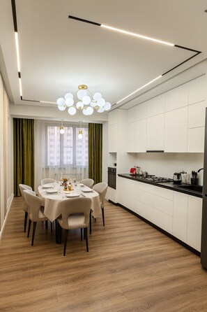 Une cuisine moderne avec des meubles blancs, un coin repas doté d’une table ronde et de chaises, et un lustre.