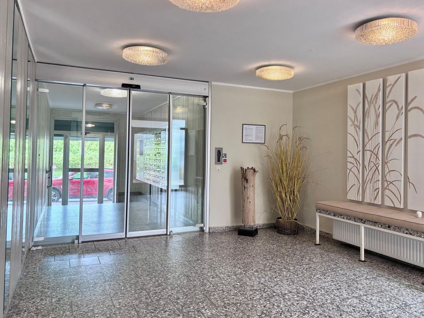 A modern lobby with a glass door entrance, a reception desk, a bench, and a wall-mounted light fixture.