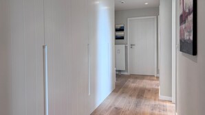 A hallway with wooden flooring, white walls, and a white door at the end. - Moin, meine Schöne - Modern 2-room apartment with luxury furnishings (Sylt)