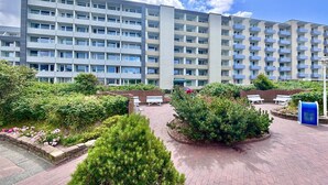 A multi-story residential building with balconies, a landscaped courtyard with benches, and a clear sky. - Moin, meine Schöne - Modern 2-room apartment with luxury furnishings (Sylt)