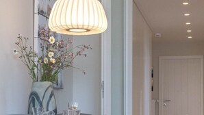 A modern dining area with a table, chairs, a hanging light fixture, and a vase with flowers. - Moin, meine Schöne - Modern 2-room apartment with luxury furnishings (Sylt)