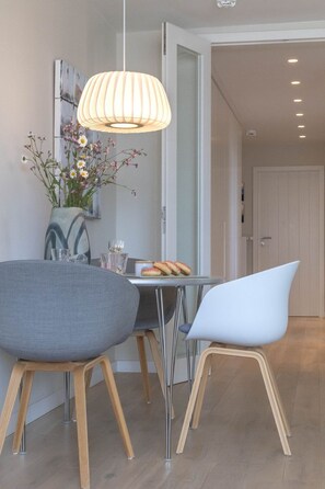 Ein moderner Essbereich mit Tisch, Stühlen, einer Pendelleuchte und einer Vase mit Blumen.