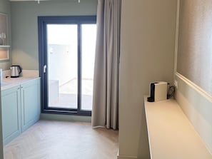 A small, well-lit room with a sliding glass door leading to an outdoor area, a kitchenette with a kettle, and a small table with a speaker. - Holiday Home - Detached (Alicante)