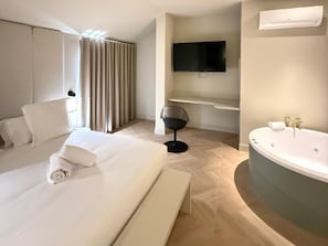 A hotel room with a large bed, a sitting chair, a flat-screen TV, a bathtub, and a window with curtains. - Holiday Home - Detached (Alicante)