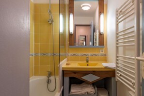 Une salle de bain avec des carreaux jaunes, une baignoire, un lavabo avec un miroir et un porte-serviettes.