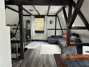 Ein Loft-Zimmer mit freiliegenden Balken, Kamin, Sofa und Esstisch.