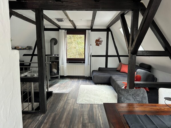 A loft-style room with exposed beams, a fireplace, a sofa, and a dining table.
