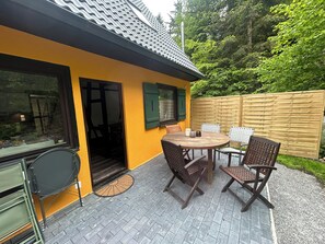 A yellow house with a tiled roof, a patio with a table and chairs, and a wooden fence.