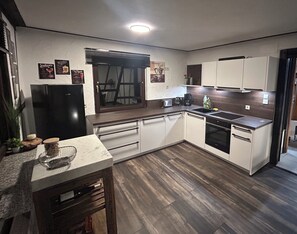 A modern kitchen with white cabinets, a black refrigerator, a built-in oven, and a window with blinds.