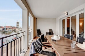 Un balcon donnant sur un port de plaisance, une table à manger en bois avec des chaises et une théière blanche.