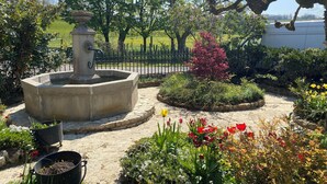 Ein Garten mit einem Brunnen, verschiedenen Pflanzen und einem gepflasterten Bereich.