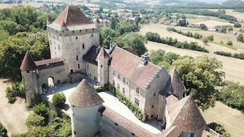Un château doté de nombreuses tours et d’une cour, entouré de verdure et de champs.