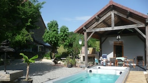Ein Whirlpool mit Holzterrasse, eine überdachte Veranda mit Gartenmöbeln und ein Kamin aus Stein.