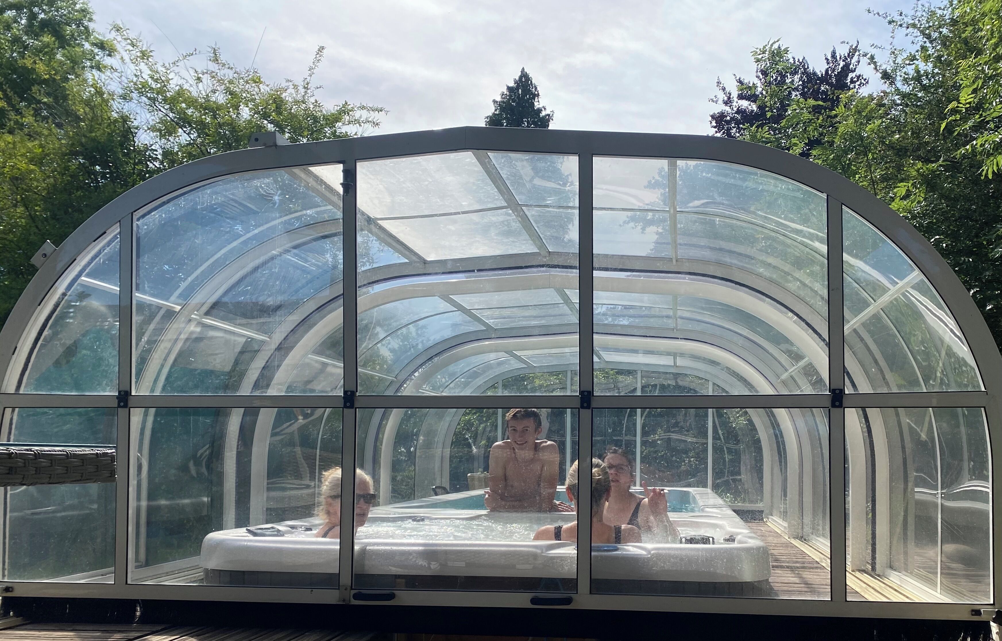Un espace abrité avec un jacuzzi, entièrement vitré et doté d’un toit incurvé, entouré d’arbres.