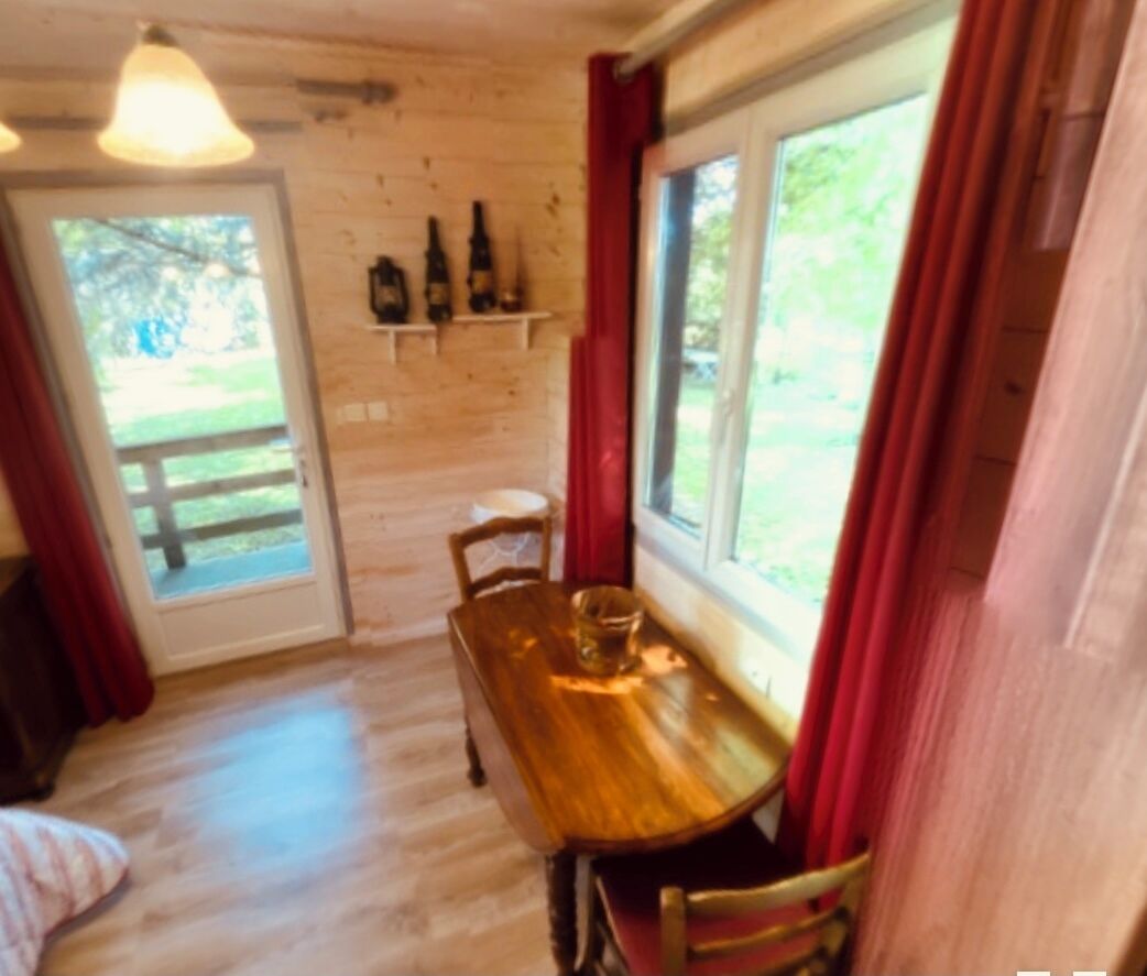 Une table à manger en bois, avec des chaises, une fenêtre avec des rideaux et une porte donnant sur l’extérieur.