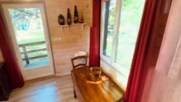 Une table à manger en bois, avec des chaises, une fenêtre avec des rideaux et une porte donnant sur l’extérieur.