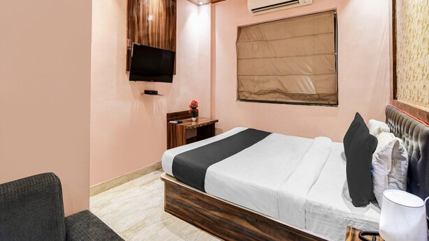 A bedroom with a bed, a TV, an air conditioner, a ceiling fan, and a window with a blind. - Deluxe Collection O Park Circus (Kolkata)