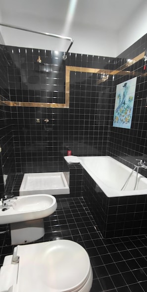 Une salle de bain avec des murs recouverts de carreaux noirs, une baignoire blanche, un lavabo blanc et des toilettes.