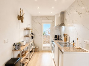 A modern kitchen with marble walls, a built-in oven, and a view through an open door. - La Goleta Apartment 5mins walk from beach (Dénia)