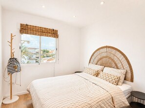 A bedroom with a bed, a window with a view, a coat rack, and a bedside table. - La Goleta Apartment 5mins walk from beach (Dénia)